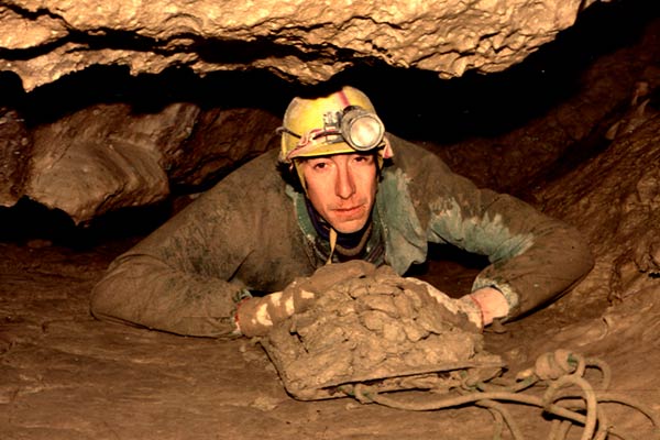 Caver excavating tight muddy passage during exploration dig in Rat's Nest Cave, Canmore Alberta — discovery of new passages in Canadian Rockies cave system