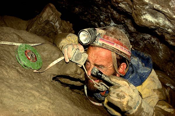 Caver taking survey measurements with tape measure in tight passage of Rat's Nest Cave, Canmore Alberta — underground mapping of Canadian Rockies cave system