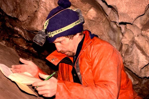 Caver recording hand-written survey notes inside Rat's Nest Cave, Canmore Alberta — underground mapping and documentation of Canadian Rockies cave system